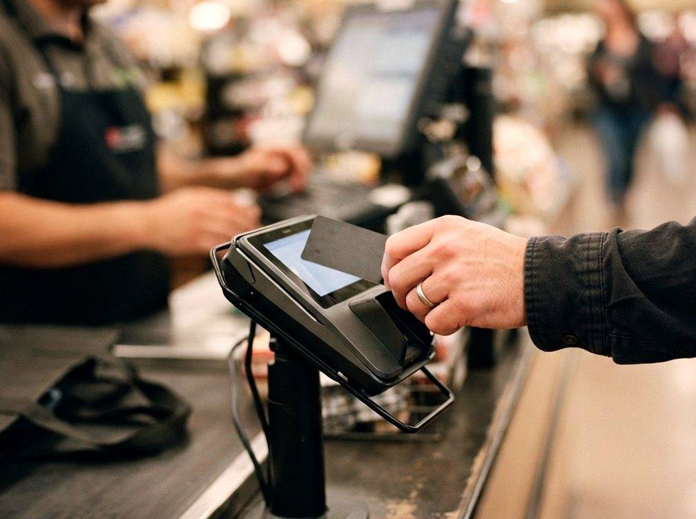 A customer taps a debit card on a payment terminal at a store checkout.