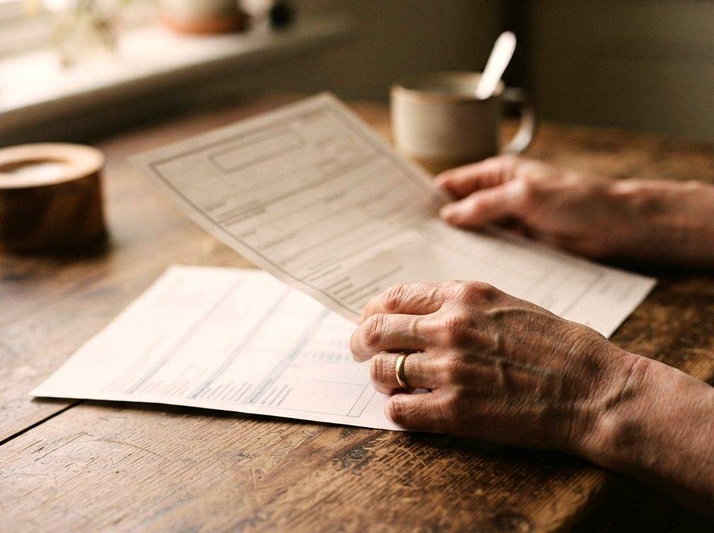 Close up of hands holding a death certificate and bank statement at a kitchen table.